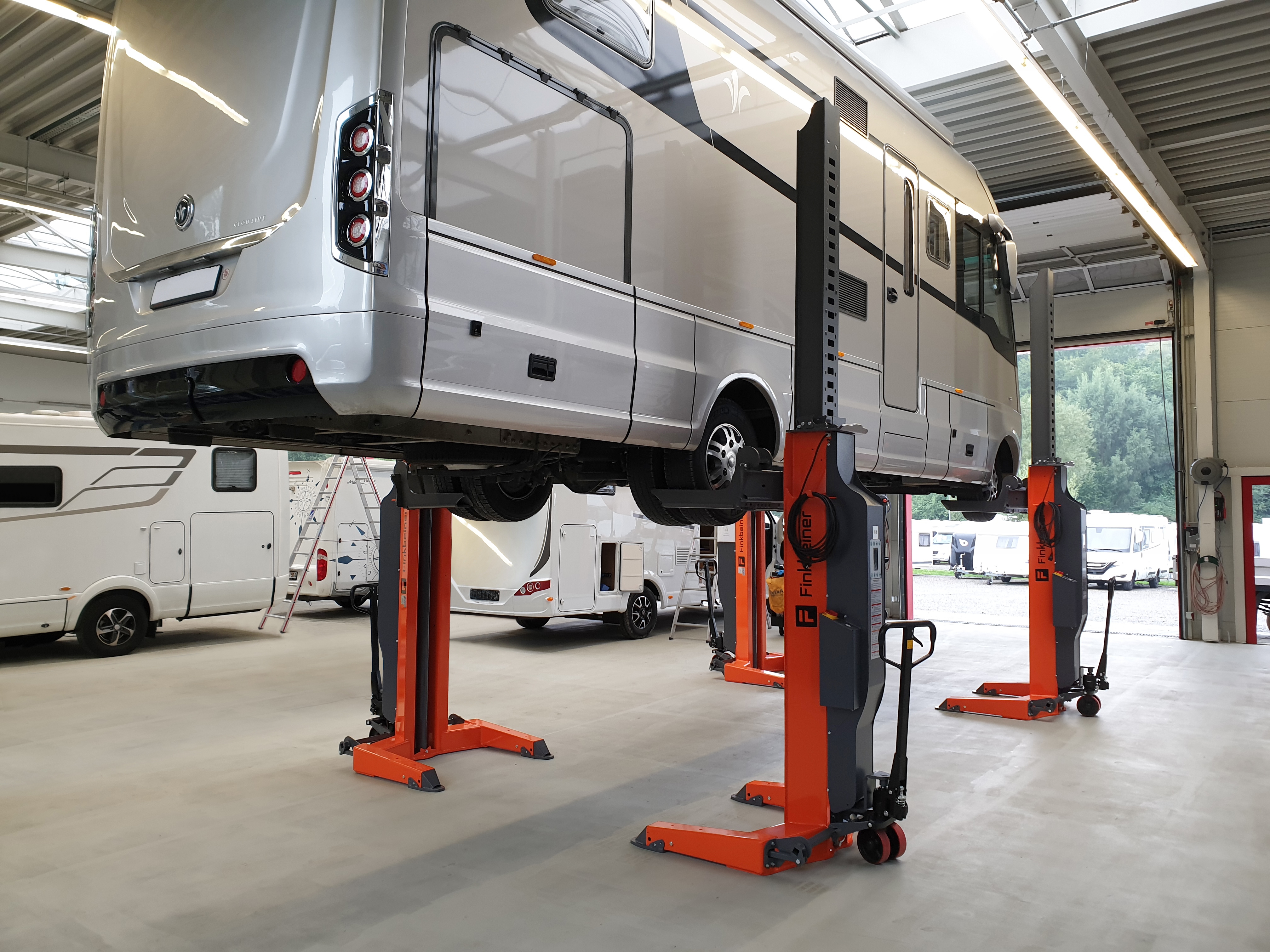 Pour effectuer une maintenance, un camping-car est soulevé à l'aide de quatre colonnes mobiles de levage dans l'atelier d'un concessionnaire.